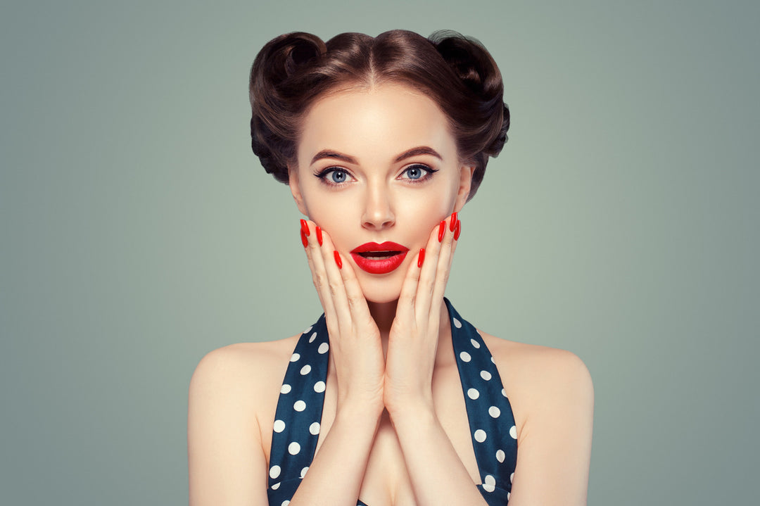 1960s woman holding manicured nails with red polish to her face. 