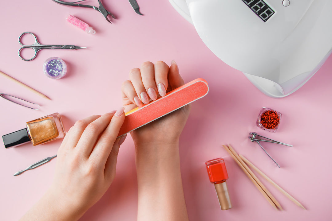 Selection of nail tools on a pink table while a nail professional is buffing nails in the foreground