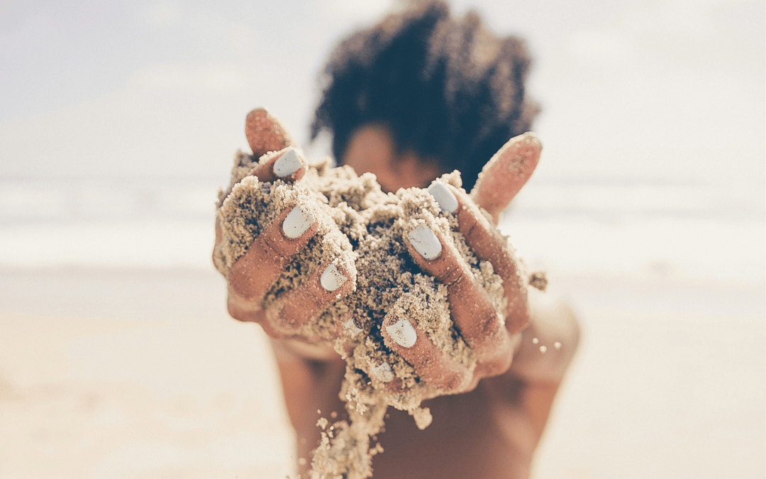 Woman with white painted nails holding sand at the beach